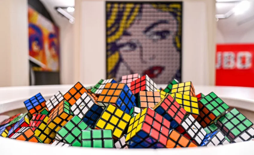 Vari cubi di Rubik e sullo sfondo un quadro di POP Art a simboleggiare le competenze in un mercato competitivo. L'immagine è all'interno di un museo.