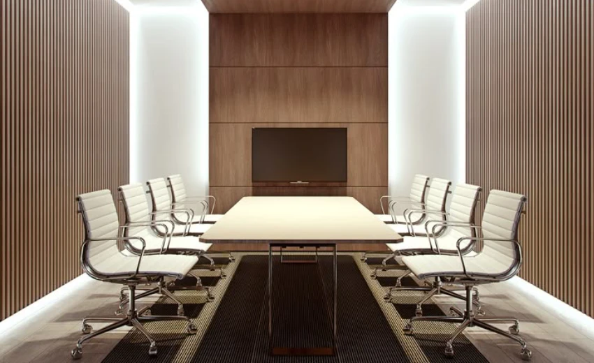 Un grande ufficio dirigenziale dell' uomo inutile con un grande tavolo ordinato, 8 sedie bianche vuota ed un televisore spendo appeso ad un muro di legno, nessuno presente.